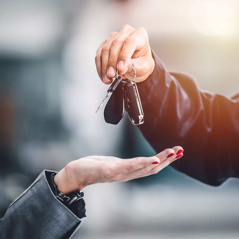 A hand holding a car key fob, while another person's hand is out, expecting to receive the key fob.